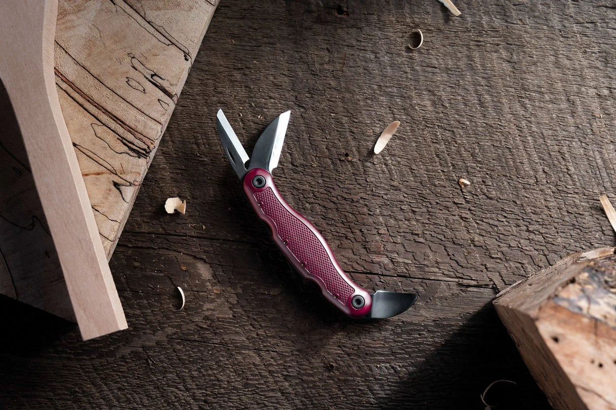 Couteau d'ébéniste multifonction à manche rouge sur table en bois, copeaux autour