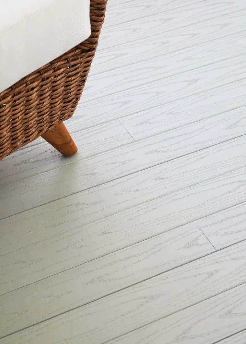 Plancher de terrasse composite gris clair effet bois, meuble en osier visible.