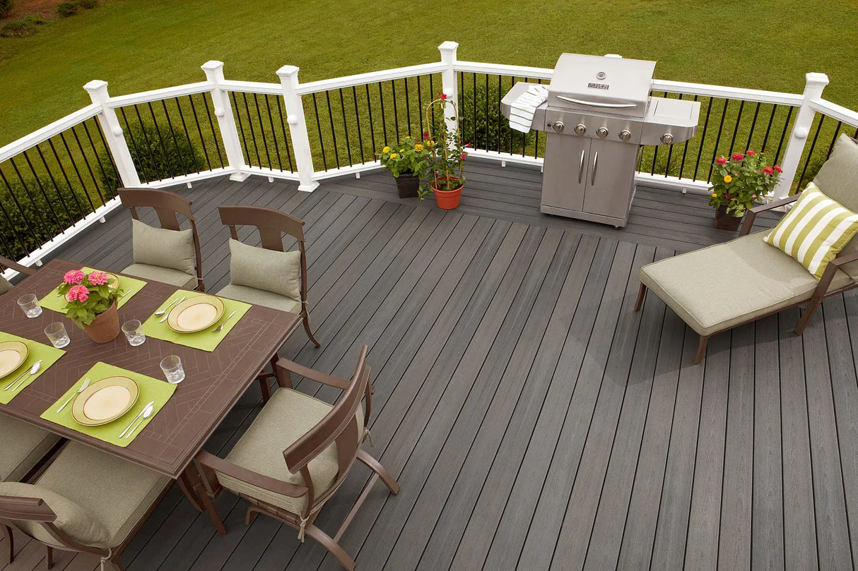 Terrasse en bois composite gris avec mobilier de jardin, barbecue et plantes, vue extérieure.