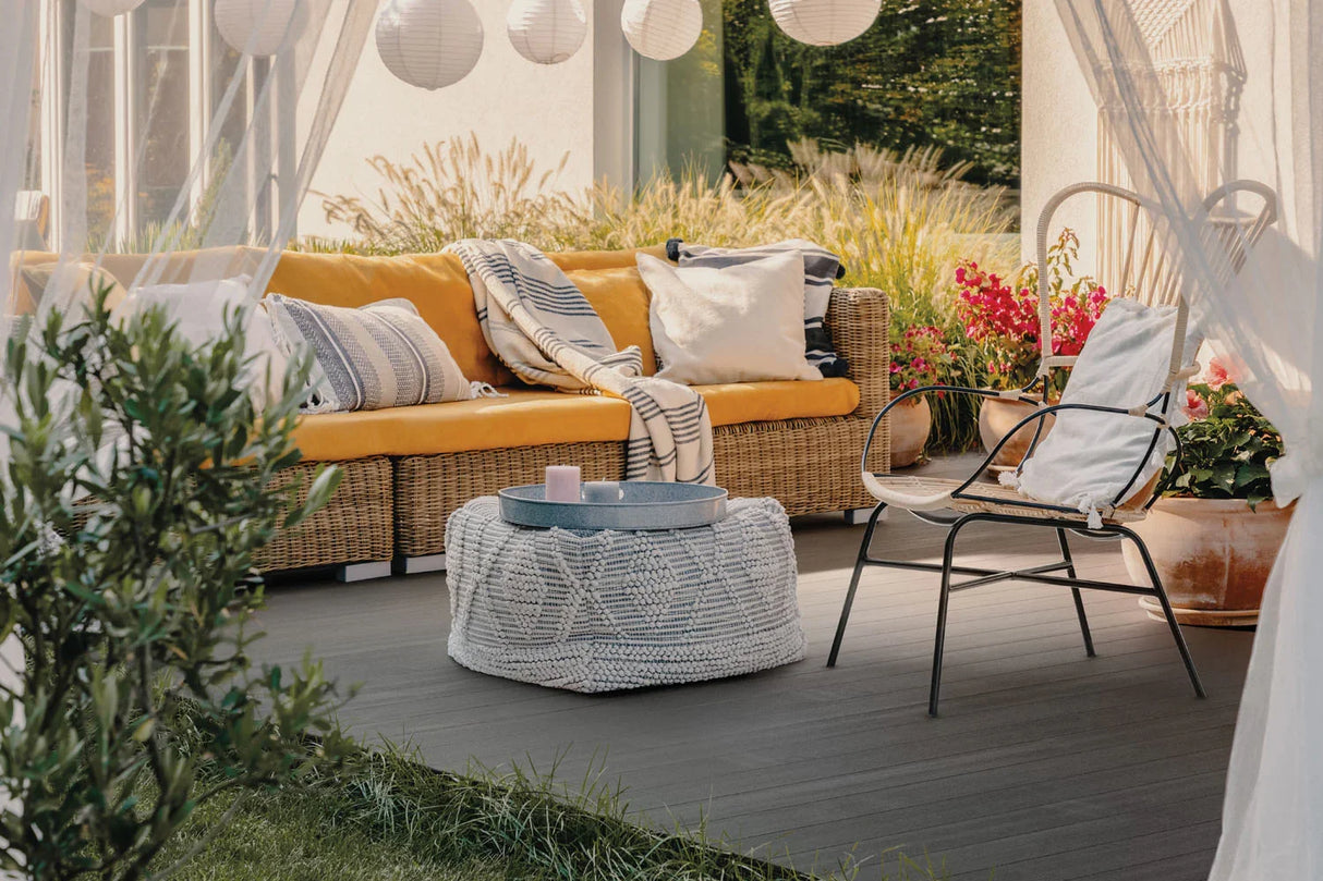 Terrasse en lames composites gris foncé avec canapé en rotin, coussins et plantes en pot