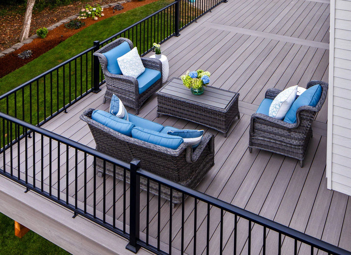 Terrasse en bois composite gris avec meubles d’extérieur et coussins bleus, rambarde noire.