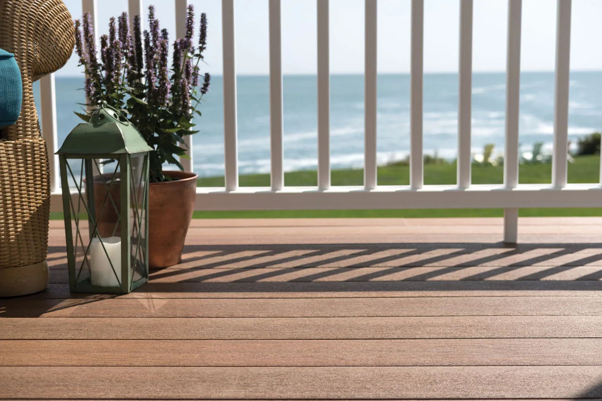 Plancher de terrasse composite brun ensoleillé avec plante et lanterne, vue sur la mer