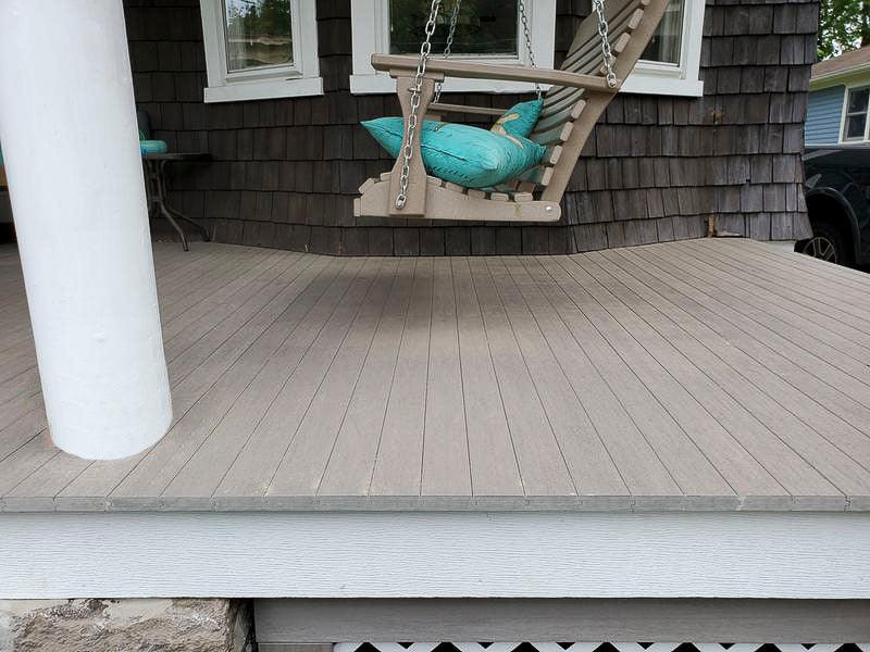Terrasse en composite gris avec balancelle en bois et coussins turquoise devant une maison.