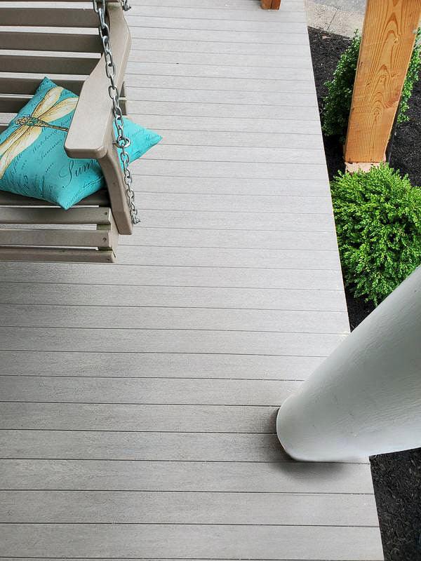 Terrasse en composite gris clair avec balancelle et coussin, poteaux en bois, arbustes décoratifs