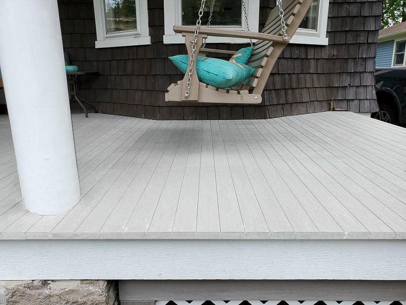 Plancher de terrasse composite gris, finition rainurée, avec une balancelle et coussins turquoise