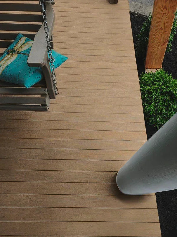 Terrasse en bois composite Weathered Teak avec banc suspendu et coussin bleu, extérieur.