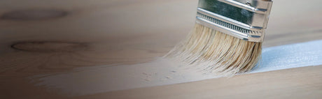 Pinceau appliquant une couche de peinture blanche sur surface en bois naturel.