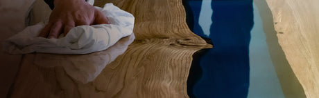 Main polissant une table en bois massif avec résine époxy bleue, finition ébénisterie