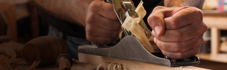 Menuisier utilisant un rabot manuel sur une planche de bois, copeaux et outils d'ébénisterie