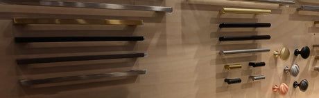 Échantillons de poignées de porte et boutons métalliques de différentes formes et couleurs sur panneau en bois.