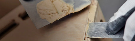 Application de pâte à bois sur une surface de bois avec une spatule pour réparation ébénisterie