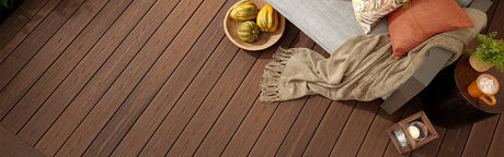 Terrasse en composite brun, décorée avec coussin, couverture et boissons, idéale extérieur.