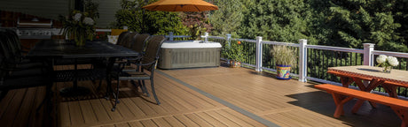 Grande terrasse en composite marron avec salon de jardin, spa, plantes et forêt en arrière-plan