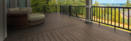 Terrasse spacieuse en composite brun foncé avec garde-corps, mobilier extérieur et vue sur jardin.