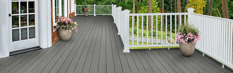 Terrasse en composite gris avec garde-corps blanc et jardinières à fleurs, vue sur jardin