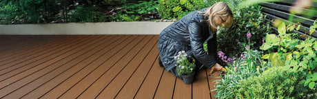 Femme jardinant à côté d’une terrasse en bois composite avec plantes vertes et fleurs