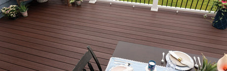Terrasse extérieure en composite brun avec plantes en pot et table dressée, lames aspect bois