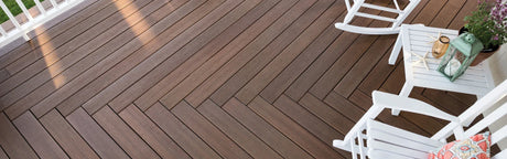 Terrasse en composite brun avec motif en chevrons, chaises blanches et table décorée