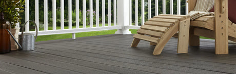 Terrasse en composite gris avec fauteuil en bois, barrière blanche et arrosoir, vue jardin