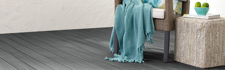 Terrasse en composite gris avec fauteuil en rotin, coussin coloré et plaid bleu