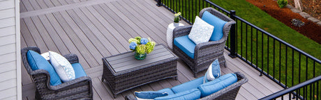 Terrasse en composite gris avec mobilier extérieur en rotin et coussins bleus, rampe noire, vue jardin