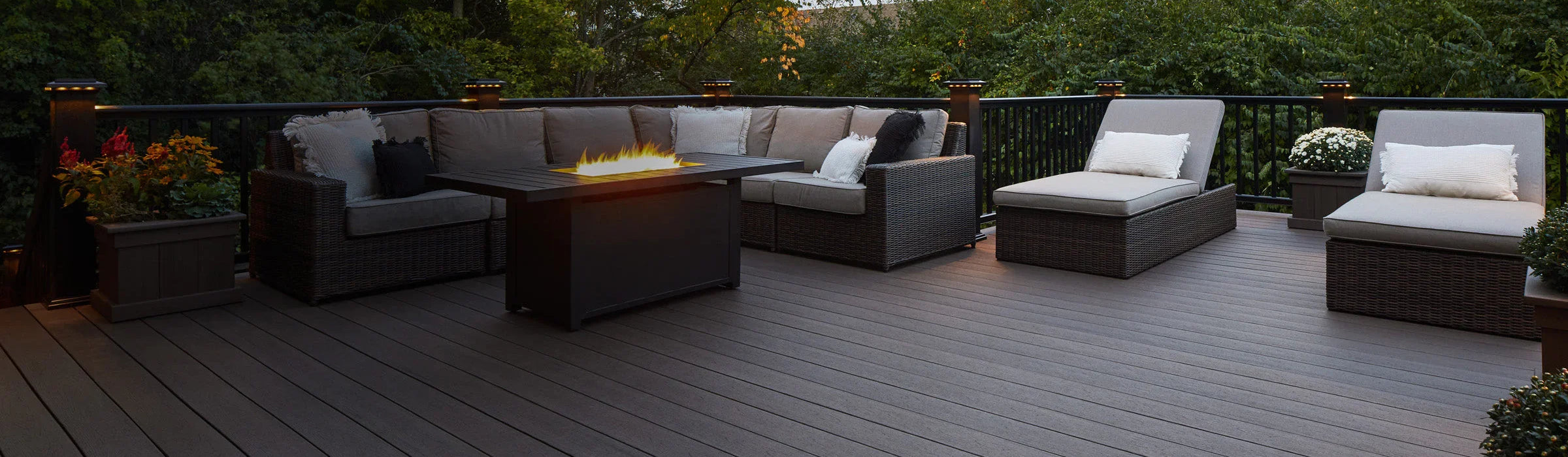 Grande terrasse extérieure en bois composite, mobilier en rotin, éclairage d'ambiance, feu de table
