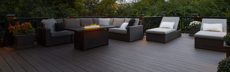 Grande terrasse extérieure en bois composite, mobilier en rotin, éclairage d'ambiance, feu de table