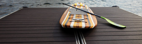 Terrasse en composite PVC effet bois foncé au bord de l’eau avec une planche de paddle.