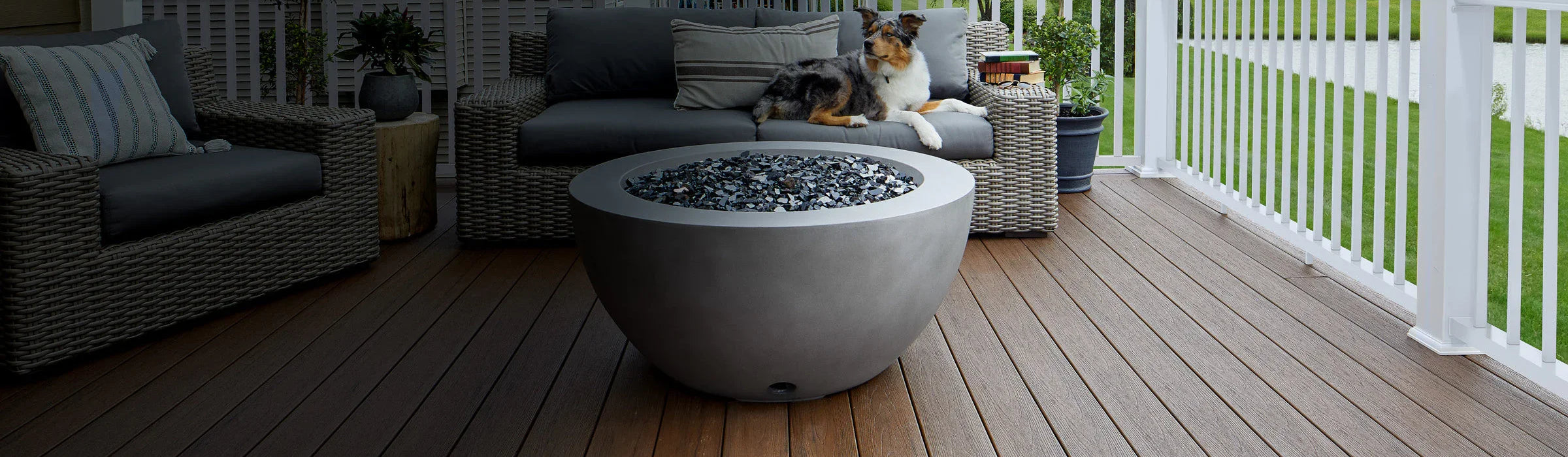 Terrasse en composite brun, canapé en rotin, grande table ronde et chien allongé