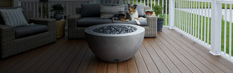 Terrasse en composite brun, canapé en rotin, grande table ronde et chien allongé