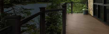 Terrasse en composite aspect bois foncé avec garde-corps, entourée d’arbres et vue sur un lac