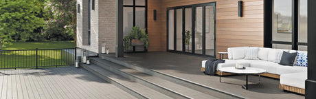 Terrasse en composite gris avec rampe noire, canapé d'extérieur et vue sur jardin