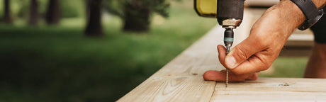 Main de bricoleur vissant une planche de bois clair pour terrasse en extérieur