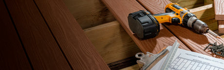 Planche de bois, perceuse et vis pour terrasse sur fond de chantier d’aménagement extérieur