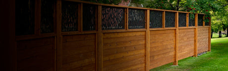 Clôture en bois avec panneaux décoratifs noirs, installée dans un jardin vert