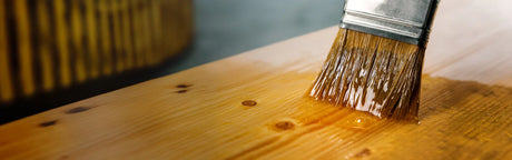 Gros plan d’un pinceau appliquant une finition sur une planche de bois pour ébénisterie.