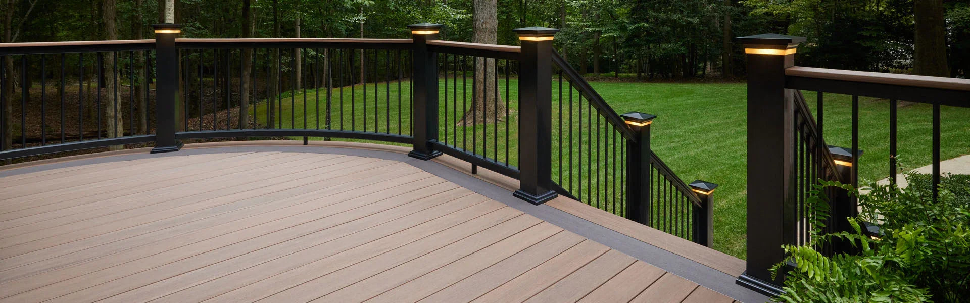 Terrasse en bois moderne avec rambarde noire, éclairage intégré et vue sur jardin verdoyant