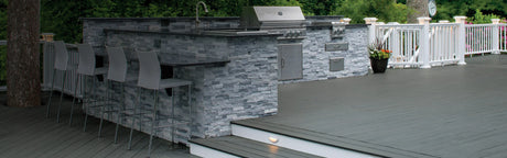 Terrasse en composite gris avec cuisine extérieure moderne, garde-corps blanc et chaises de bar
