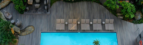 Terrasse en bois composite gris autour d'une piscine, chaises longues et végétation luxuriante