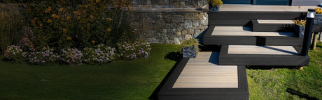 Escalier de terrasse composite gris foncé avec jardinières et pelouse, devant un mur de pierre