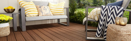 Terrasse en composite brun avec mobilier de jardin, coussins et fleurs, ambiance extérieure chaleureuse