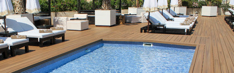 Terrasse en bois composite brun autour d’une piscine, avec chaises longues et parasols