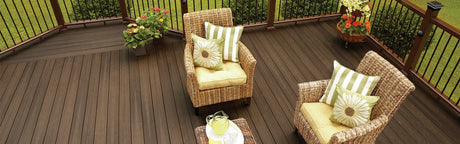Terrasse extérieure en composite brun foncé avec fauteuils en rotin, fleurs et coussins décoratifs