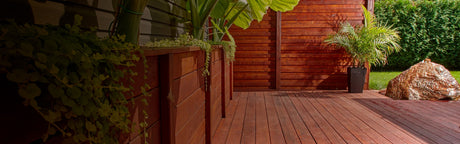 Terrasse en bois exotique avec jardinières et plantes vertes, clôture en bois et pelouse