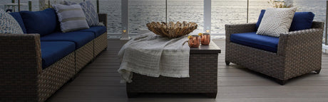 Terrasse en composite gris avec mobilier en rotin, coussins bleus et vue sur l'eau