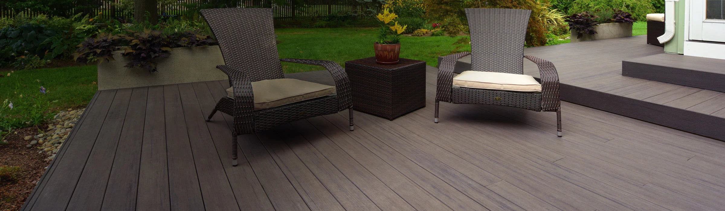 Terrasse en composite brun avec fauteuils en rotin, table basse et vue sur jardin verdoyant