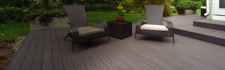 Terrasse en composite brun avec fauteuils en rotin, table basse et vue sur jardin verdoyant
