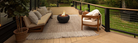 Terrasse en bois composite teck vieilli avec fauteuils, foyer extérieur et plantes vertes